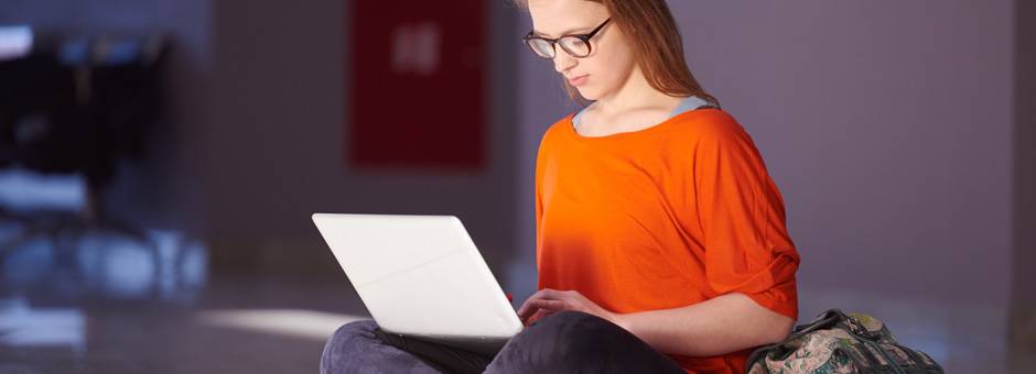 Student in orange shirt looks at white laptop