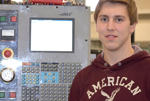Male student standing in-front of a CNC machine operating panel